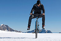 Ein Mann fährt mit dem Fahrrad im Schnee, die Füsse hält er in die Höhe