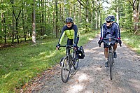 Velojournal hat Hartmut Ortlieb für ein seltenes Gespräch getroffen. Zwei Männer fahren auf Fahrrädern auf einem Kiesweg im Wald. 