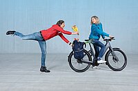 Ein Mann mit roter Jacke steht auf einem Bein und reicht einer Frau einen Blumenstrauss