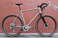 Citycycles Perfetto Gravelbike. Gravelbike aus Titan vor roter Mauer. 
