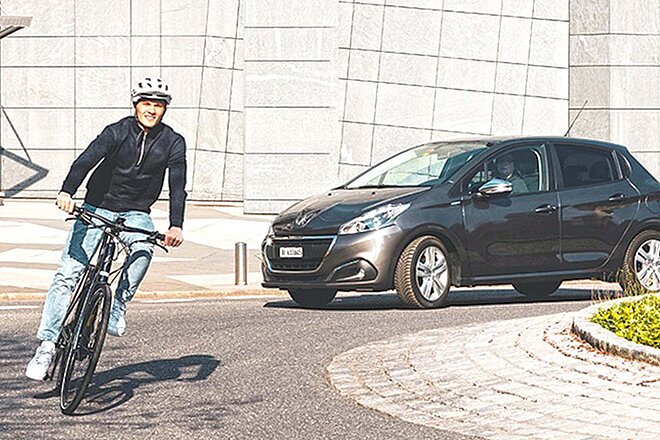 Ein Mann fährt mit dem Fahrrad durch einen Kreisverkehr, ihm folgt ein Auto.