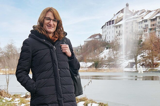 Eine Frau mit Winterjacke steht vor einem Teich