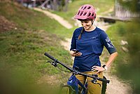 Bosch Update Smart System. Eine Bikerin mit blauem Shirt und rosa Helm blickt auf ihr Smartphone.