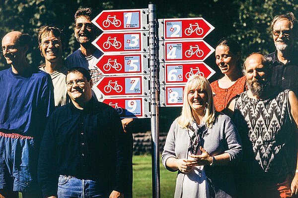 Eine Gruppe vom Personen steht neben einem Wegweiser.