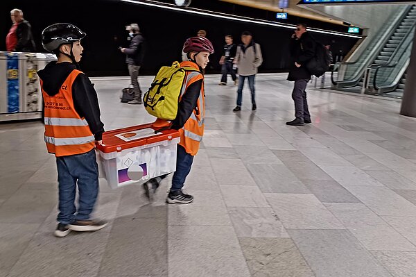 Zwei Kinder tragen eine Kuriersendung am Züricher Hauptbahnhof.