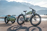 Ateliers Heritage Bike. Vintage E-Bike mit Anhänger steht vor einem See.