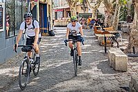 Ein Mann und eine Frau mit weissen Shirts radeln über Kopfsteinpflaster.
