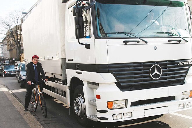 Ein Radfahrer steht am Strassenrand neben einem LKW.