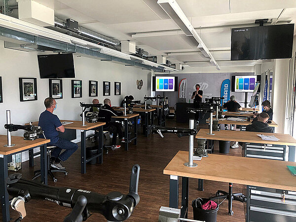 Kurs als Velomechaniker Quereinsteiger. Personen sitzen in einem Schulungsraum an Tischen.