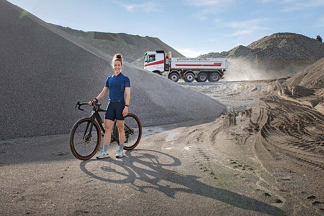 Die aktuellen E-Gravelbikes sind leicht und flink und damit auch Trendsetter für künftige E-Alltagsvelos. Eine junge Frau steht mit einem Gravelbike in einer Kiesgrube.