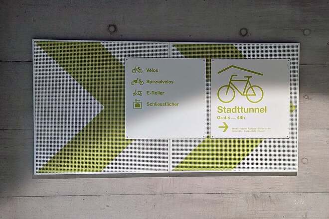 Schild, das Radfahrenden den Weg zu einem Veloparking weist. 