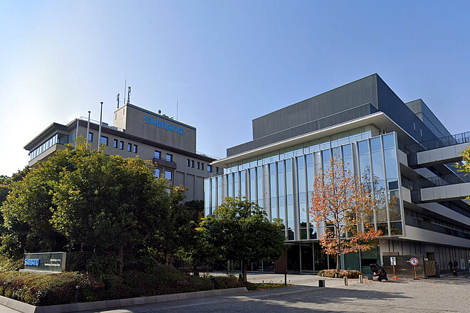 Firmengebäude mit Glasfront, im Vordergund ein Baum.