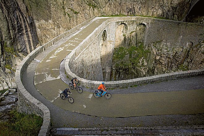 Mit dem E-Bike über die Alpen. Drei Personen fahren mit E-Bikes auf einer alten Passstrasse. 