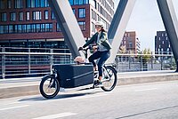 E-Bikes 2023. Die besten Modelle des Jahres. Eine Frau transportiert ein Kind auf einem Cargobike von Riese & Müller.