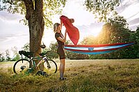 Tipps draussen schlafen auf der Velotour. Eine Frau in Fahrradbekleidung steht neben einer Hängematte.