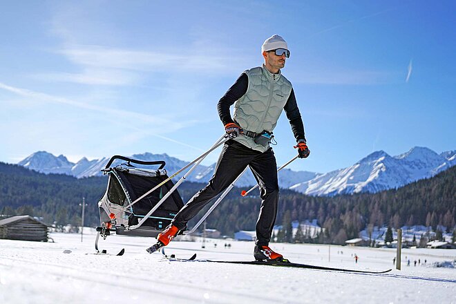 Ein Mann fährt auf Langlaufski und zieht einen Schlitten hinter sich her.