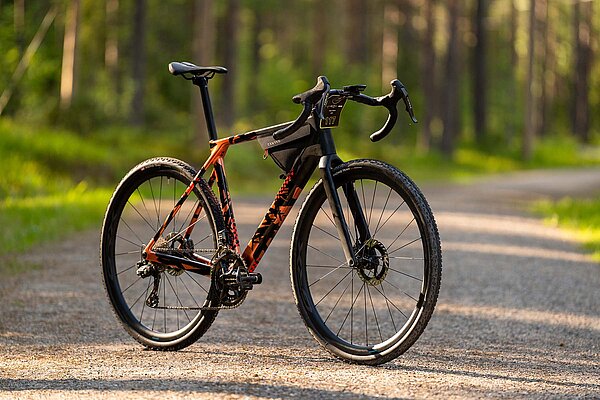 Ein Gravelbike steht auf einem Schotterweg. Im Hintergrund ist ein Wald zu sehen.