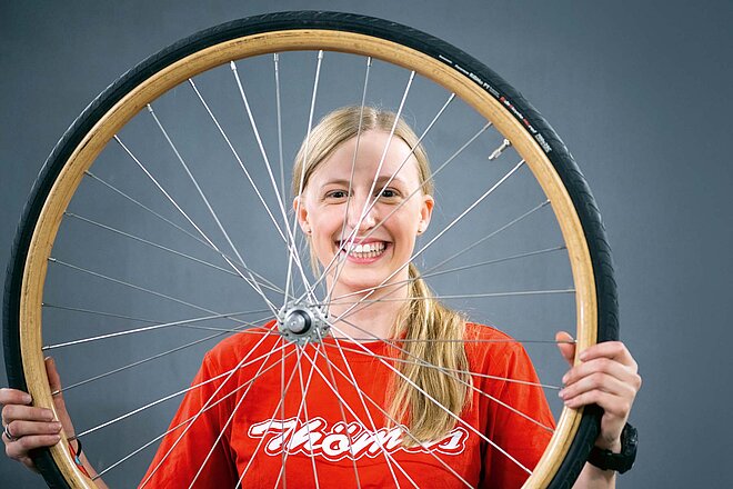 Eine Frau hält ein Fahrradrad in die Höhe.