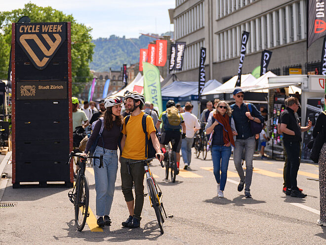 Ein Mann und eine Frau laufen händchenhaltend mit Velos auf einem Weg. 