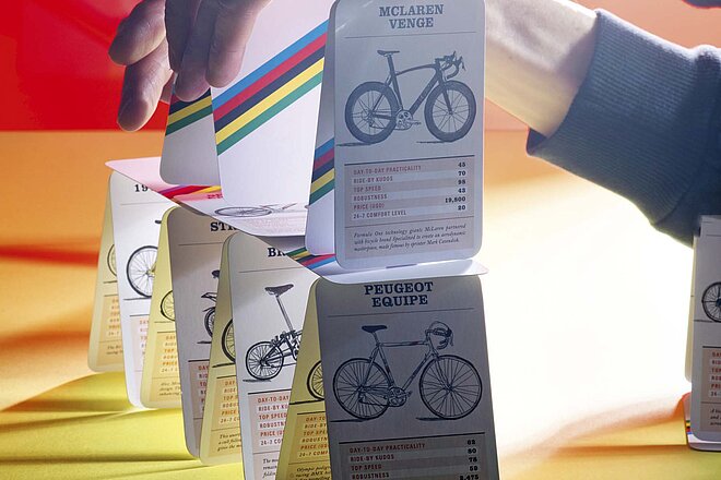 Ein Velokilometer kostet mehr, als man denkt. Ein Velokilometer kostet mehr, als man denkt. Kartenhaus mit Quartettkarten, auf denen Velos zu sehen sind.