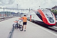 Ein Velokurier schliesst die Sendung im Zug ein.