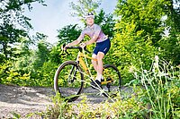 Eine Frau mit buntem Fahrradtricot fährt auf einem Gravelbike im Wald.