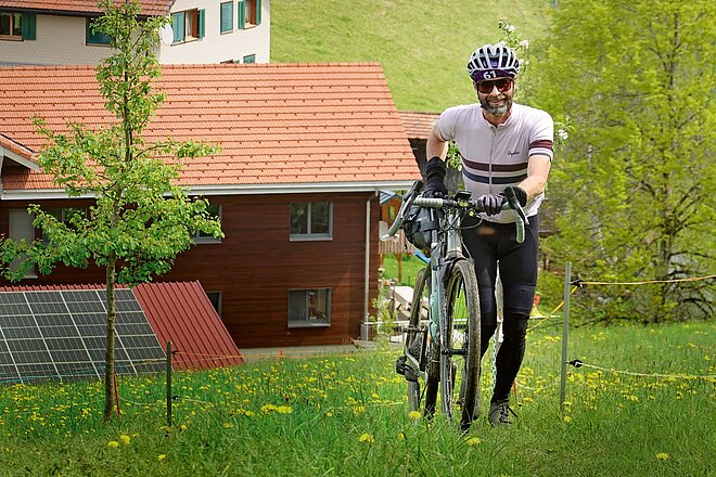 Gravelbike Rennen Lucerne 303. Ein Mann schiebt sein Fahrrad einen Hang hinauf.