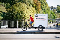 Vernehmlassung Cargobikes. Ein Mann im roten T-Shirt fährt auf einem Lastenrad.
