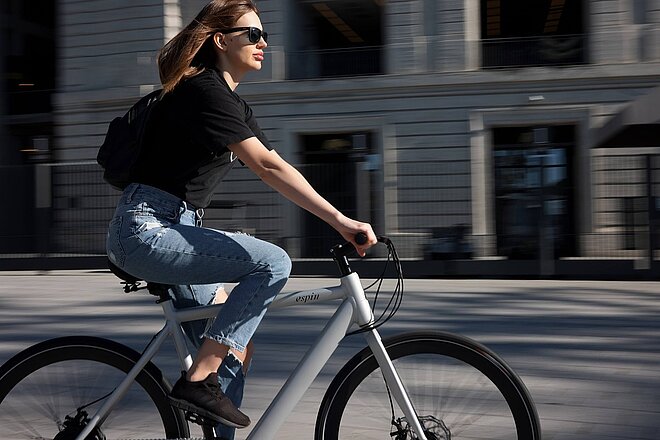 Tipps für den Occasionskauf eines E-Bikes. Eine junge Frau mit schwarzem T-Shirt fährt auf einem E-Bike.